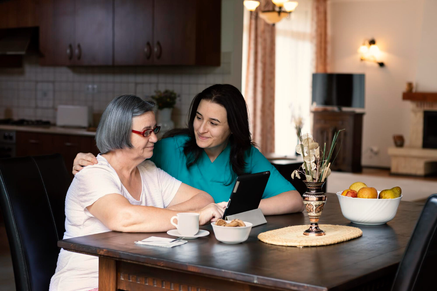 Female caregiver sits in the kitchen with an elderly woman
