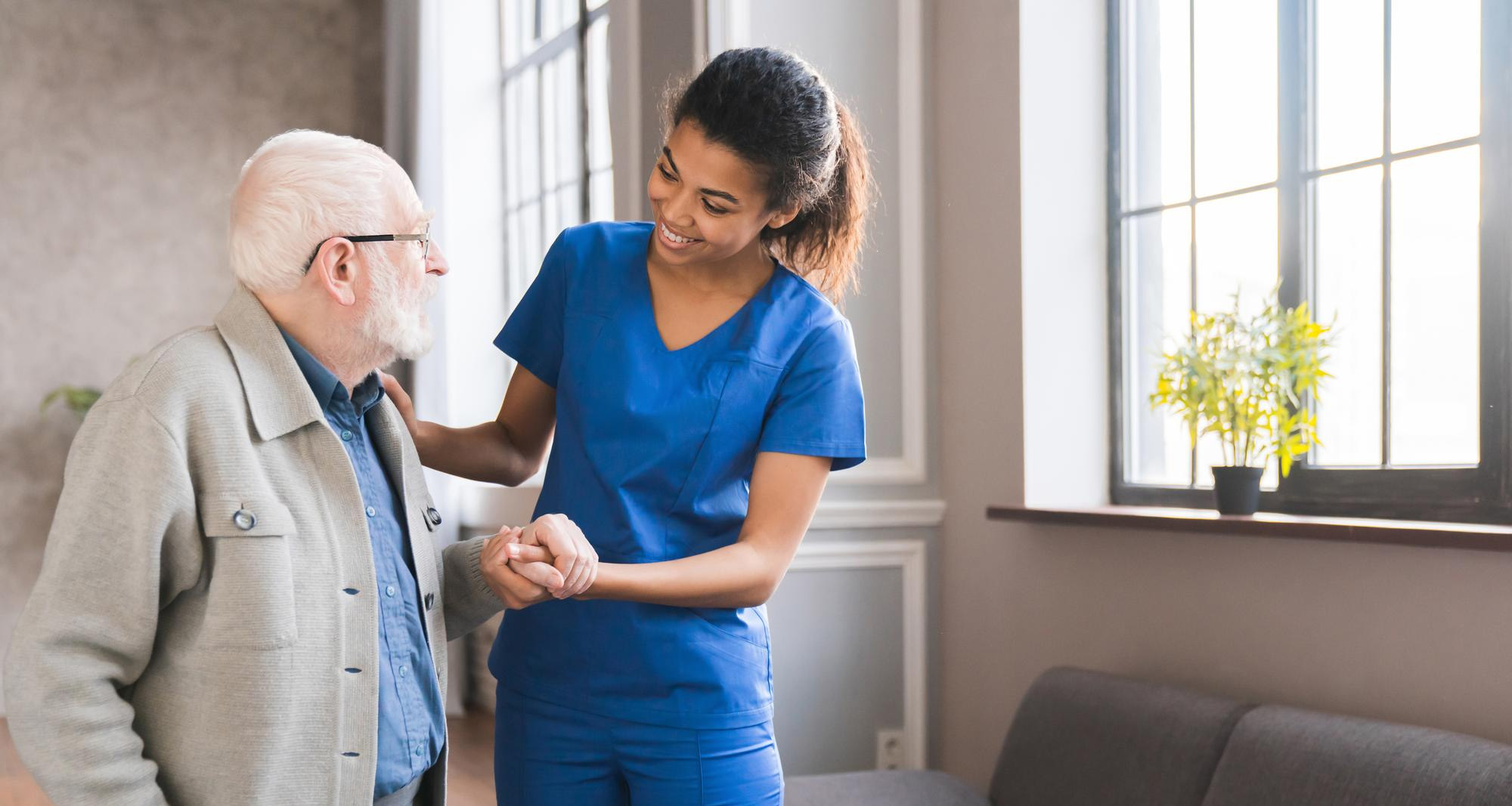A caregiver helping an elderly man by the hand